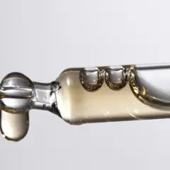 Tropfen eines goldenen Serums, das Bisabolol enthält, fallen aus einer Pipette.