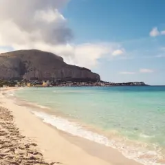 Piękna plaża Mondello z turkusową wodą, piaszczystym brzegiem i malowniczym miasteczkiem w tle.