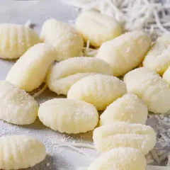 Frische Gnocchi, bereit für köstliche Gnocchi Rezepte, liegen auf einem grauen Untergrund, bestreut mit etwas geriebenem Käse.