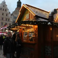 Tłum ludzi na największym jarmarku bożonarodzeniowym w Polsce. Drewniana budka z lampkami, w tle karuzela.