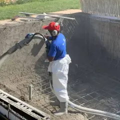 Un ouvrier projette du béton pour créer un bassin en béton étanche. La structure métallique est visible.