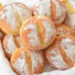 Koszyk pełen świeżych, puszystych bułek ziemniaczanych, posypanych mąką. Idealne na śniadanie.