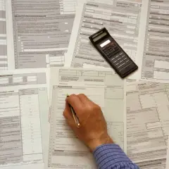 Hand füllt Steuerformulare aus, ein Taschenrechner liegt bereit. Die Dokumente zeigen verschiedene Anlagen und Abschnitte, die für die Berechnung von vorsorgeaufwendungen steuer relevant sind.
