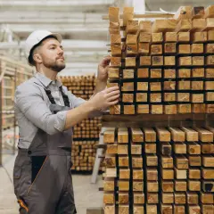 Pracownik w kasku sprawdza drewno na magazynie. To dowód na indywidualną produkcję na zamówienie.