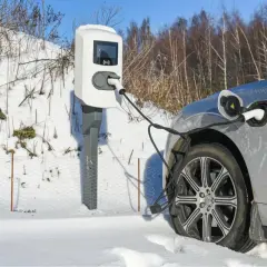 Une voiture électrique grise est branchée à une borne de recharge dans un paysage enneigé. Le chauffage de la voiture électrique est assuré par cette connexion.