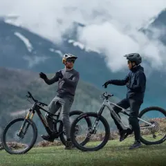 Dos ciclistas con cascos y bicicletas ebike en un paisaje montañoso, listos para explorar nuevas rutas.
