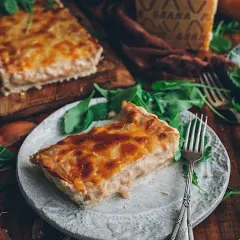 Una rebanada de tarta de cebolla dorada y cremosa, servida con rúcula fresca y un trozo de queso.
