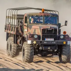 Kraz 255 z załogą przemierza piaszczysty teren, wzbijając tumany kurzu.