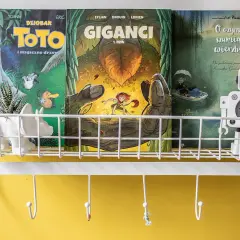 Na półce stoją komiksy do nauki czytania: "Toto i magiczne drzewo", "Giganci" i "O czym szumią wierzby". Obok robot-zegarek.