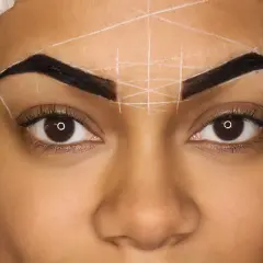 Zbliżenie na twarz kobiety z zaznaczonymi henną brwiami i białymi liniami do geometrii.