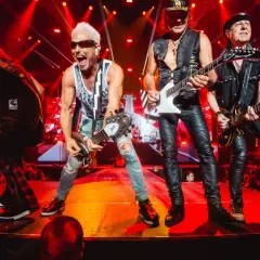 Zespół Scorpions na koncercie, grający swoje rockowe ballady. Wokalista z blond włosami i w okularach krzyczy do mikrofonu.