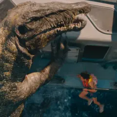 En enorm dinosaurie klättrar upp på en farkost i det nya Jurassic Park, med en liten flicka hängande vid räcket.