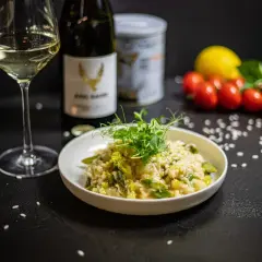 Kremowe risotto z kurczakiem i szparagami, udekorowane kiełkami. Obok kieliszek białego wina i butelka.