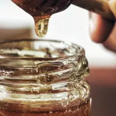 Goutte de miel doré tombant d'une cuillère dans un pot en verre. Une délicieuse alternative par quoi remplacer le sirop d'érable.
