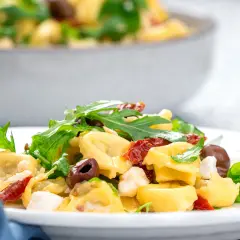Ein Teller mit Tortellinisalat mit Rucola, sonnengetrockneten Tomaten und Oliven.