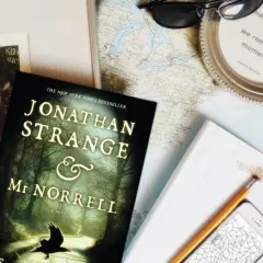 Książka "Jonathan Strange i Pan Norrell" leży obok mapy, telefonu i okularów, gotowa na podróż pełną magii.
