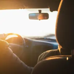Två personer i en bil i solnedgången. Föraren håller i ratten. Vad betyder begagnad? Kanske bilen är begagnad, men resan är ny.