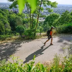 Persona con mochila camina por un sendero, disfrutando del senderismo y las vistas de la ciudad.
