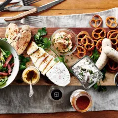 Ein rustikales Brett mit klassischen deutschen Gerichten: Weißwurst, Brezeln, Käse, Salat und Brot.