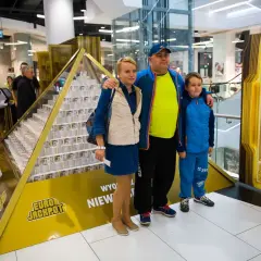 Rodzina pozuje przy piramidzie z pieniędzy, symbolizującej wygraną w Eurojackpot. Dowiedz się, eurojackpot jak odebrać wygraną.