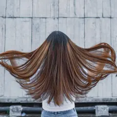 Lange, braune Haare mit honigfarbenen Strähnen, die sich im Wind bewegen. Ein perfekter Look für die sommer trend haarfarben.