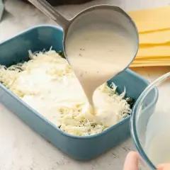 Se vierte bechamel para lasaña sobre queso rallado en un molde azul.