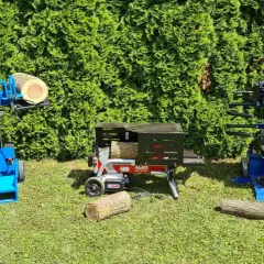 Zwei Holzspalter, einer davon mit Einhandbedienung, stehen im Gras vor einer grünen Hecke.