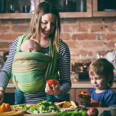 Mama z dzieckiem w chuście i synem przygotowują posiłek. Od kiedy można nosić dziecko w chuście? Od pierwszych dni życia!
