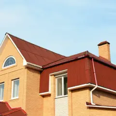 Jasna mansarda z cegły, z czerwonym dachem i kominem, pod błękitnym niebem.
