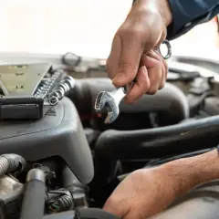 Mechanik dokonuje wymiany sprężarki klimatyzacji, używając klucza do odkręcenia śrub w silniku samochodu.
