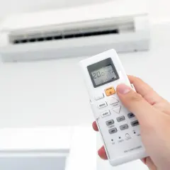 Mano sujetando un control remoto de aire acondicionado, ajustando la temperatura para combatir el calor o el frío.