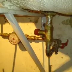Instrukcja jak zamontować zawór bezpieczeństwa przy bojlerze. Widoczny wodomierz i instalacja wodna.