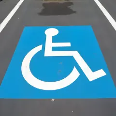 Symbole de fauteuil roulant blanc sur fond bleu, marquant une place de stationnement réservée. Une amende place handicapé est une infraction.