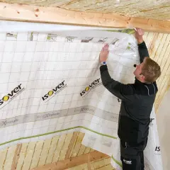 Montaż folii paroprzepuszczalnej od wewnątrz. Pracownik mocuje membranę Isover Vario XtraSafe na poddaszu, zabezpieczając izolację.