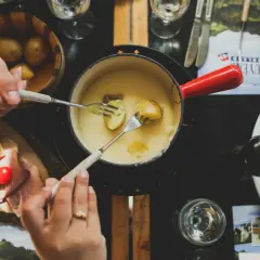 Des mains trempent des pommes de terre dans une fondue savoyarde, un délice de fromages fondus suisses.