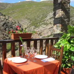 Mesa puesta para comer en Patones de Arriba, con vistas a un valle montañoso. Flores y plantas decoran el balcón.