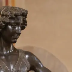 Brązowa rzeźba młodego mężczyzny z kręconymi włosami, patrzącego w bok.
