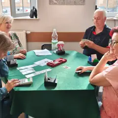 Cztery osoby grają w brydża dla początkujących przy zielonym stole.