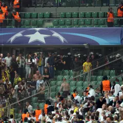 Tłum kibiców na trybunach, wśród nich stewardzi w kamizelkach i policja w hełmach. Atmosfera napięcia, jakby zaraz mieli wybuchnąć kibole.