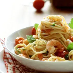 Ein Teller mit köstlichen Spaghetti mit Garnelen, Kirschtomaten und frischem Basilikum, appetitlich angerichtet.
