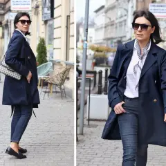 Elegancka kobieta w granatowym trenczu damskim, białej bluzce w paski i jeansach spaceruje po brukowanej ulicy.