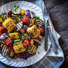 Assortiment coloré de légumes plancha : courgettes, maïs, poivrons, tomates cerises et oignons rouges grillés, assaisonnés d'herbes.