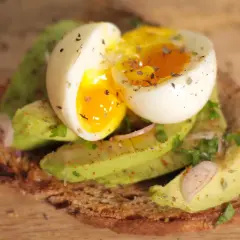 Tartine oeuf et avocat, un délice crémeux avec un jaune coulant, garnie d'herbes fraîches et d'épices sur du pain grillé.