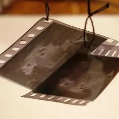 Klisze filmowe wiszą na sznurku, czekając na wywołanie. Zdjęcia przedstawiają stare samochody.