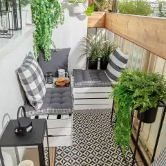 Przytulny balkon w bloku z wygodnymi siedziskami z palet, mnóstwem zieleni i czarno-białymi dodatkami. Idealne miejsce na poranną kawę.