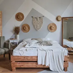 Przytulna sypialnia w stylu boho z łóżkiem z drewna, makramą na ścianie i słomianymi kapeluszami.