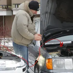 Mężczyzna próbuje odpalić auto zepsutym rozrusznikiem, używając kabli rozruchowych.