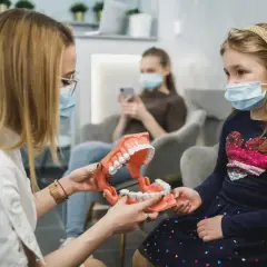 Ortodonta wyjaśnia dziecku budowę szczęki na modelu. W poczekalni siedzą inne osoby.