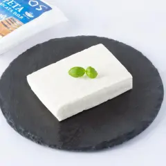 Un blocco di feta DOP su una pietra scura, guarnito con basilico. La confezione è visibile sullo sfondo.