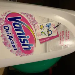 Butelka płynu Vanish Oxi Action Crystal White z etykietą i zawieszką informującą o działaniu.